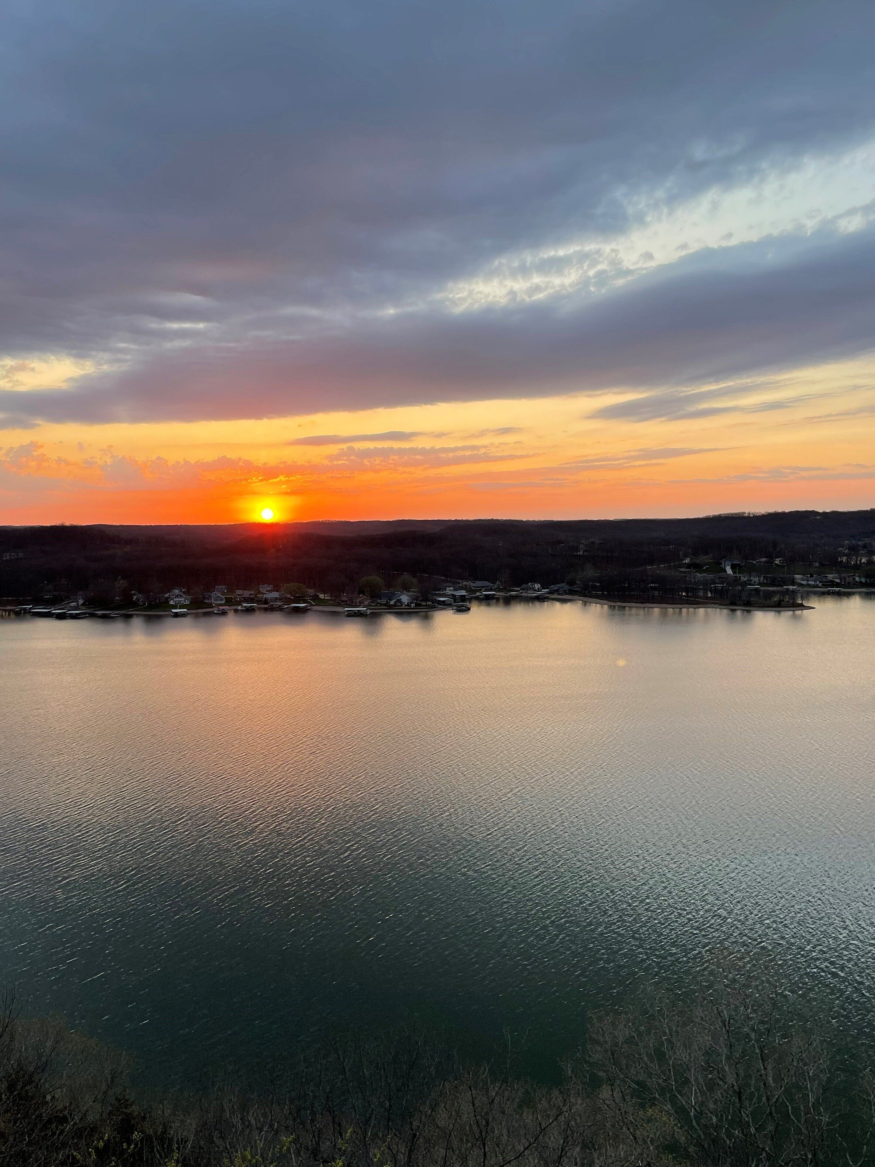 Un coucher de soleil sur un lac paisible, avec une rive lointaine.