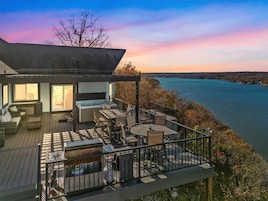 Um terraço com móveis de exterior, vista para um lago e um edifício com grandes janelas.