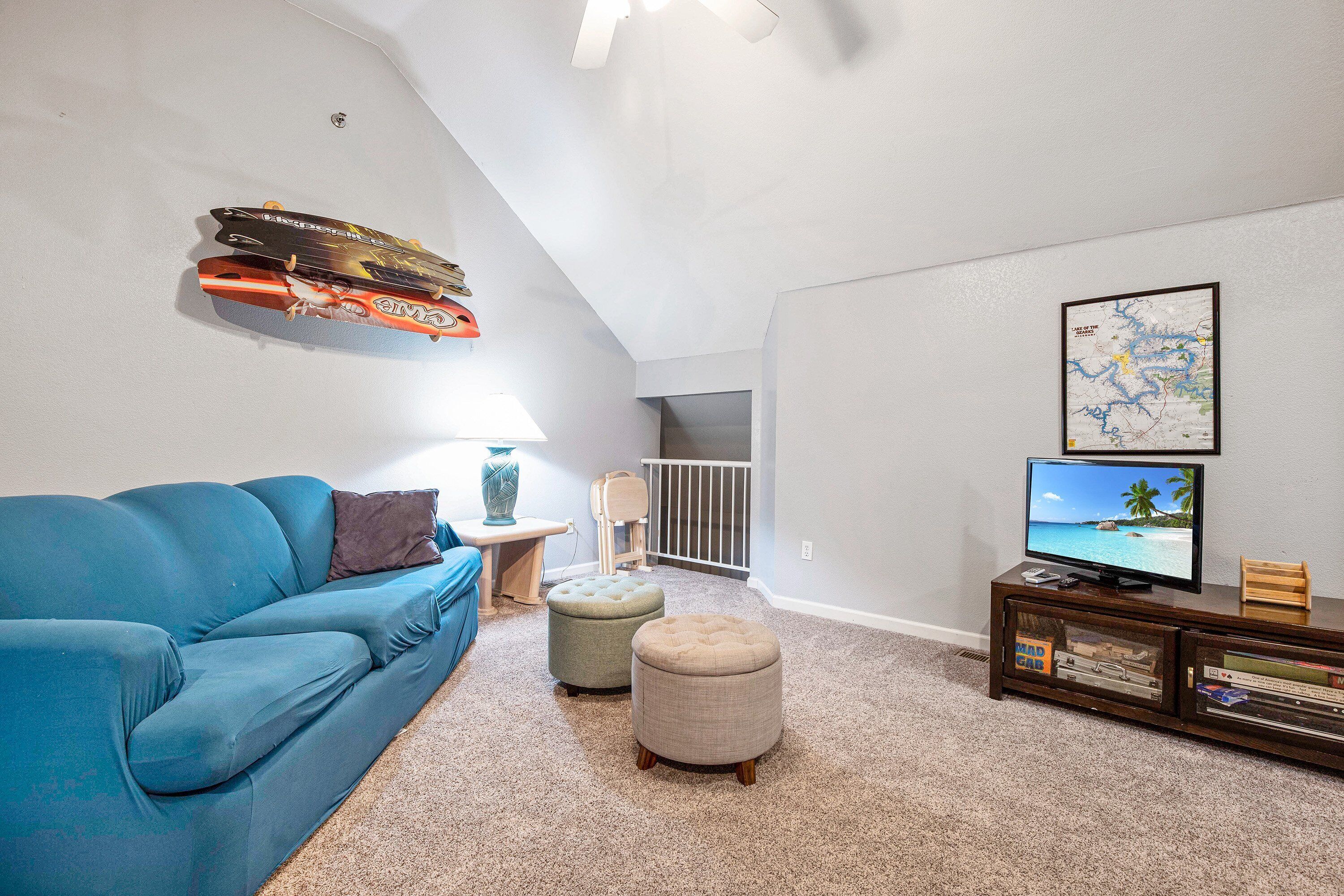 A living room with a blue sofa, two ottomans, a TV on a wooden stand, and a map on the wall.