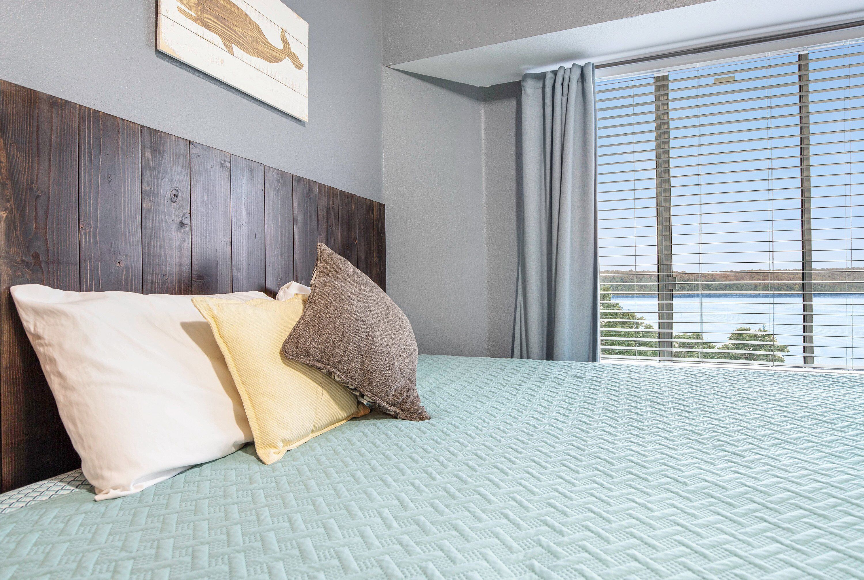 Ein Schlafzimmer mit einem großen Bett, einem Holzkopfende und Blick auf ein Gewässer durch das Fenster.