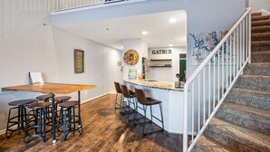 A modern kitchen with a wooden island and bar stools, a staircase, and a sign that reads "GATHER". - Penthouse Living In The Heart of the State Park (Kaiser)