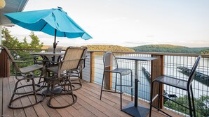 A wooden deck with a table and chairs, a blue umbrella, and a view of a lake and hills. - Penthouse Living In The Heart of the State Park (Kaiser)