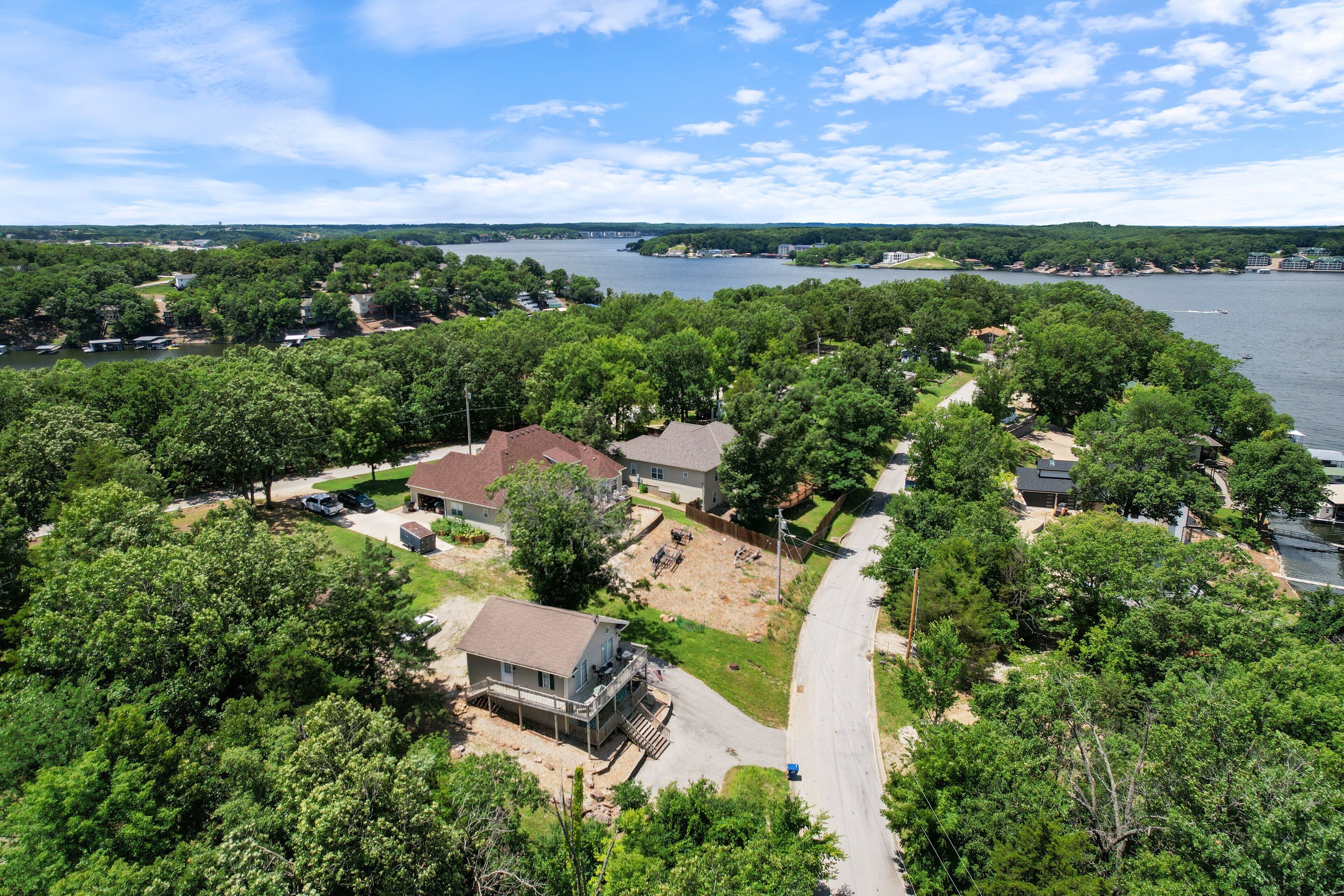 A residential area with houses surrounded by dense trees, a clear sky, and a body of water in the background.