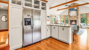 A modern kitchen with white cabinets, a stainless steel refrigerator, and a stone fireplace. - Amazing Cove, Fenced Yard, & Game Room! (Sunrise Beach)