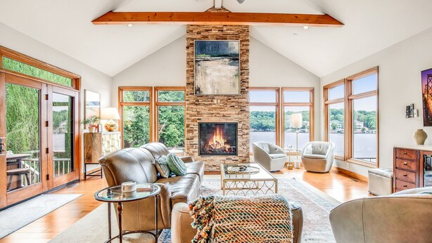 A spacious living room with a fireplace, leather furniture, large windows, and a view of the outdoors. - Amazing Cove, Fenced Yard, & Game Room! (Sunrise Beach)