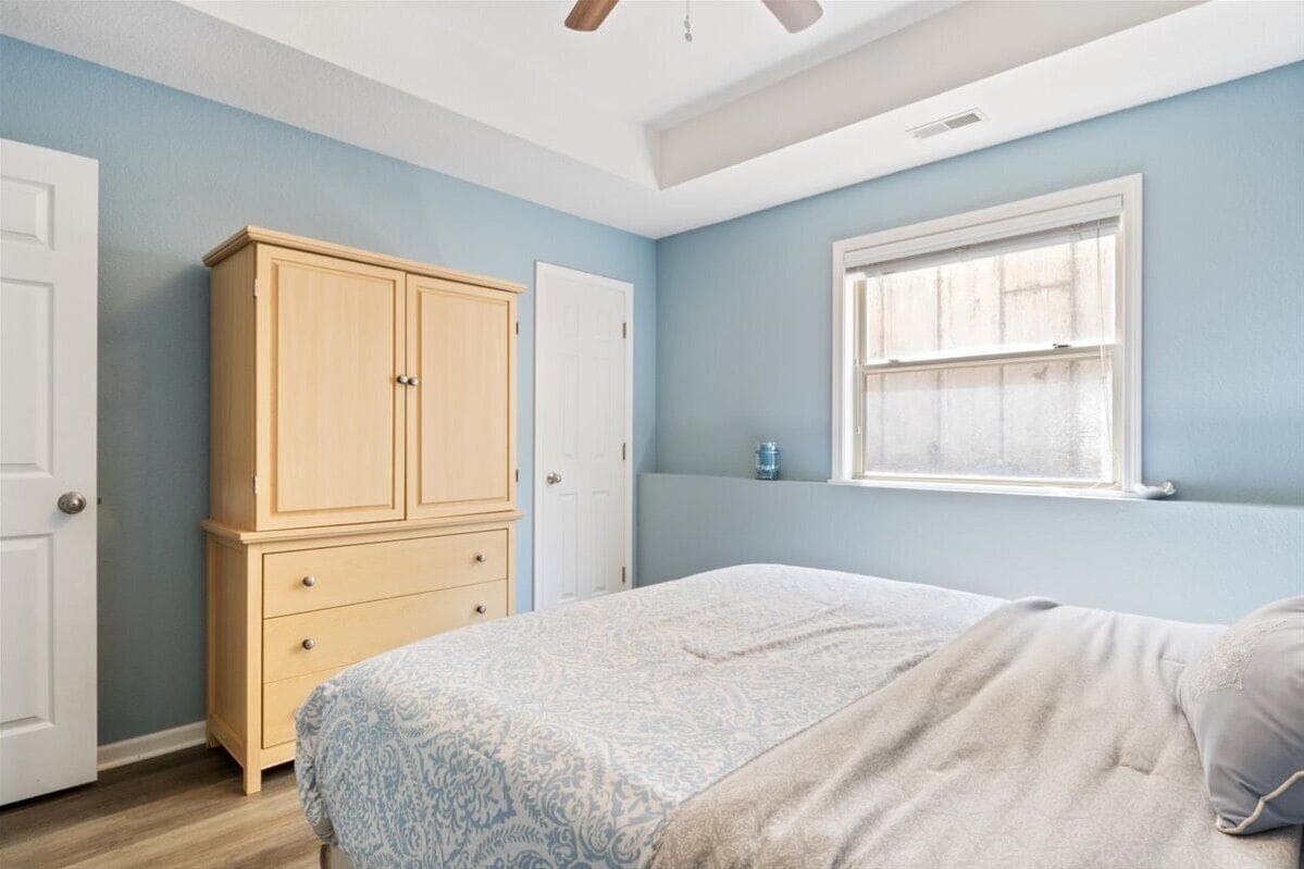 Ein Schlafzimmer mit Bett, Schrank, Fenster und Deckenventilator.