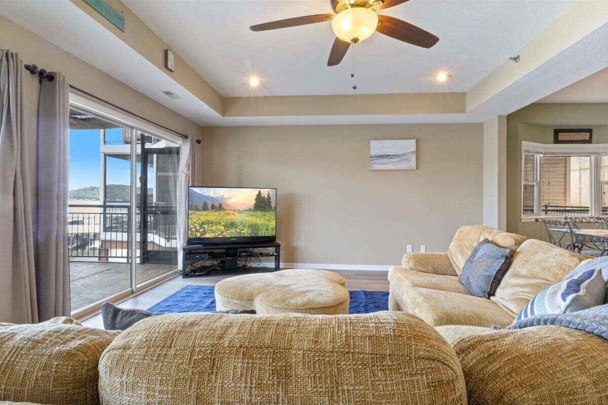 A living room with a television, sofa, ottoman, ceiling fan, and a view through a sliding glass door.
