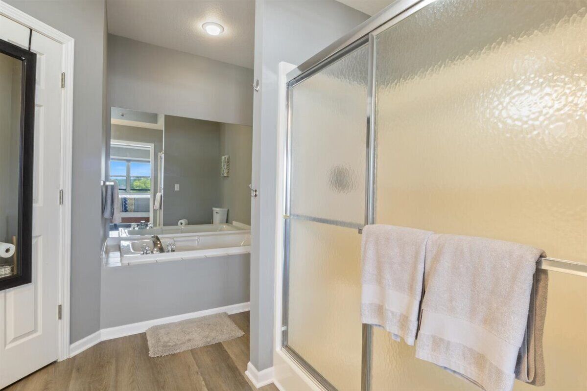 A modern bathroom with a glass shower enclosure, a large mirror, and a bathtub.