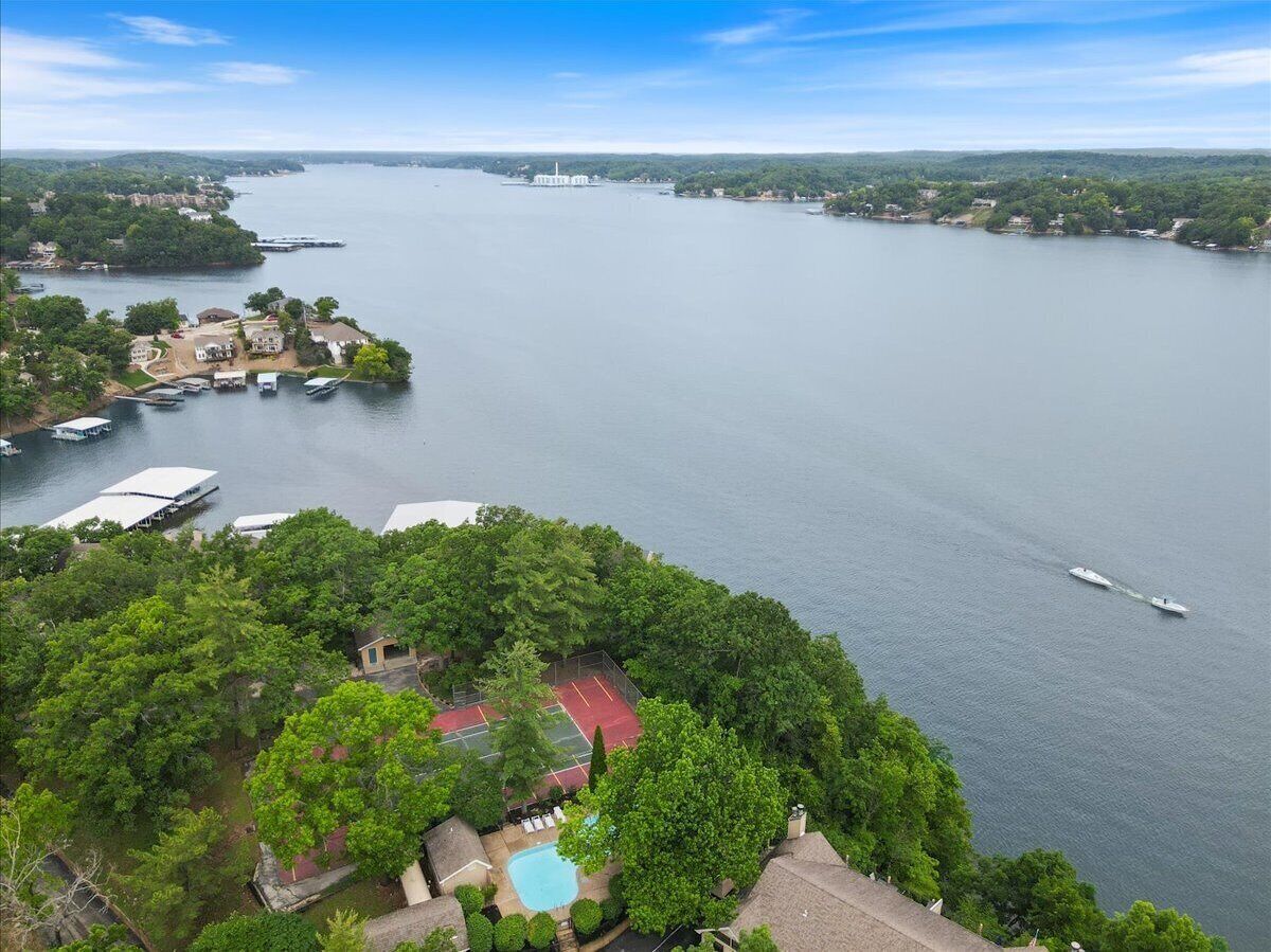 A lakeside property with a tennis court, a swimming pool, and boats docked near the shore.