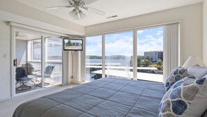 A bedroom with a large bed, a ceiling fan, a TV, and a balcony with a view of the city. - Games, Lake Views, Ease of Access to Unit & Attractions, Family-friendly, Outdoor Comfort (Lake Ozark)