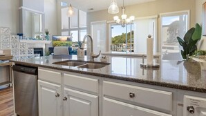 Une cuisine moderne dotée de plans de travail en granit, de meubles blancs, d’appareils électroménagers en acier inoxydable et de luminaires suspendus.