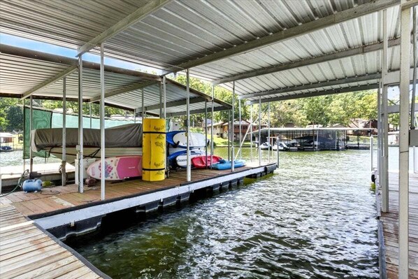 A covered dock with a boat and kayaks, a water pump, and a green tarp. - Lakefront Home w/ Dock, Boat Slip, Private Ramp, Kayaks, Paddle Boards & Firepit (Sunrise Beach)