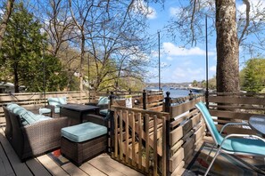 Une terrasse extérieure aménagée avec des meubles en osier, une table et des chaises, donnant sur une étendue d’eau.