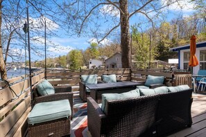 Une terrasse extérieure avec des meubles en osier, une table et une vue sur un plan d’eau et des maisons en arrière-plan.