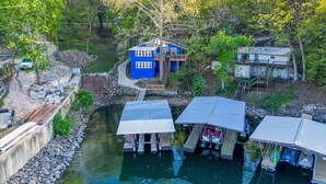 A riverside property with a blue house, docked boats, and a small dock area.