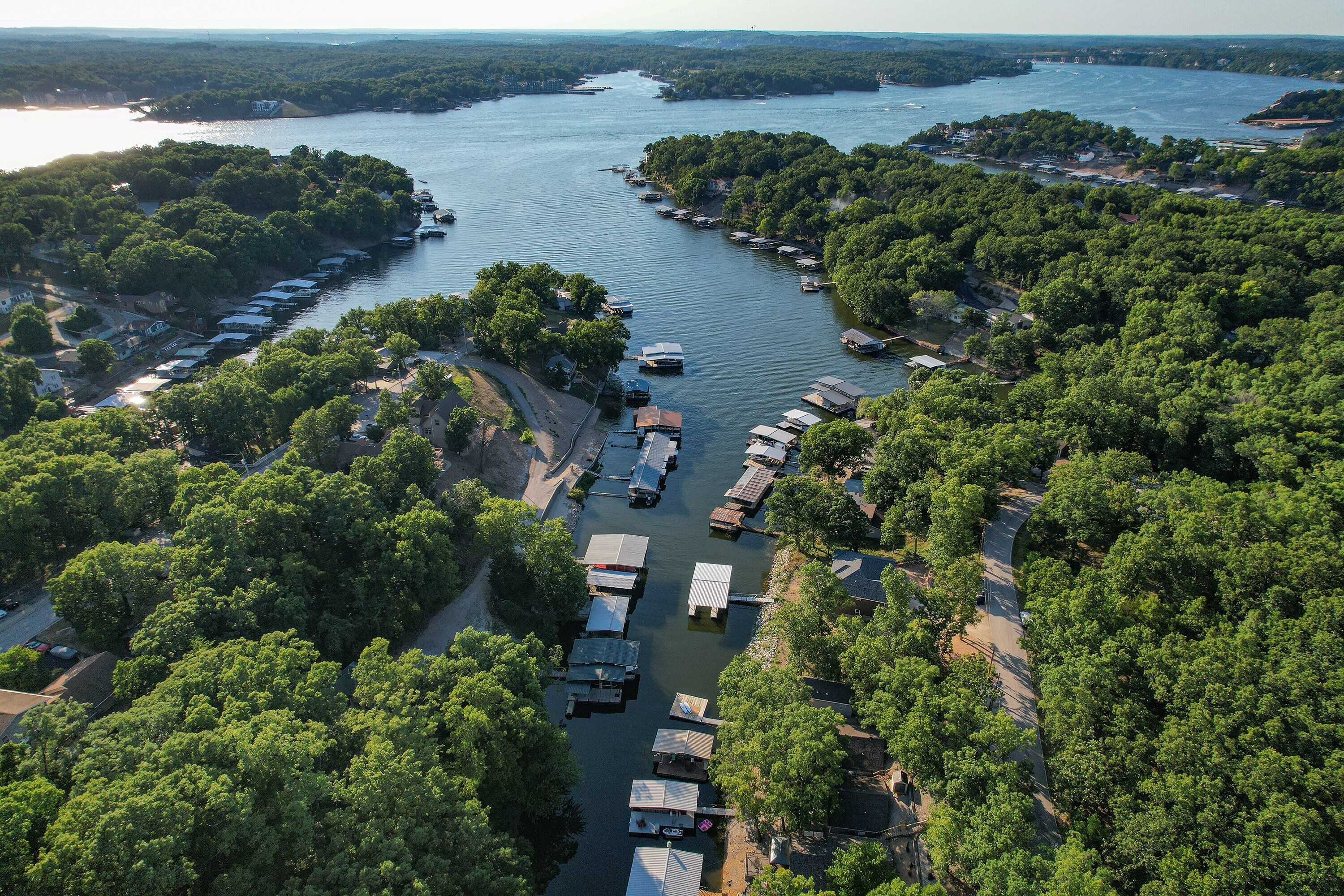An aerial view of a lakeside campground with numerous RVs and boats docked along the shoreline, surrounded by dense forest.