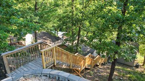 A wooden deck with a staircase leading to a covered area, surrounded by trees. - Private Dock, Paddle Boards, Views & Hot Spots! (Osage Beach)