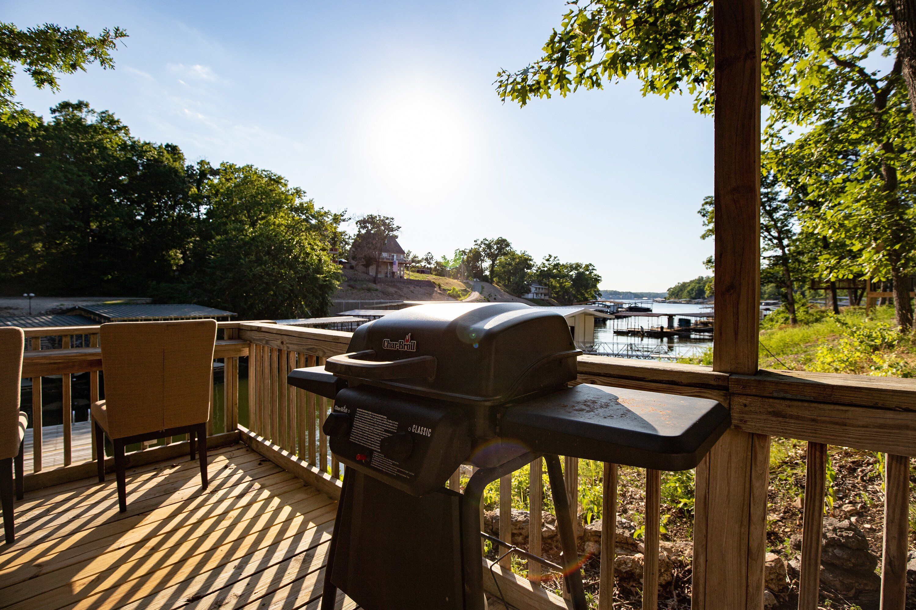 Une terrasse équipée d’un barbecue Char-Broil, de chaises et offrant une vue sur un plan d’eau et des bâtiments situés au loin.