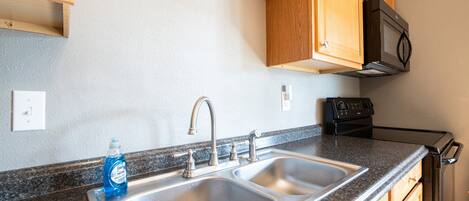 Una cocina con un lavamanos doble, armarios de madera, un microondas y un grifo de acero inoxidable.