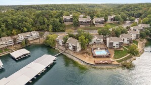 A lakeside residential area with multiple two-story houses, a dock, and a swimming pool area. - Poolside Condo With Amazing Lake Views & Design (Osage Beach)