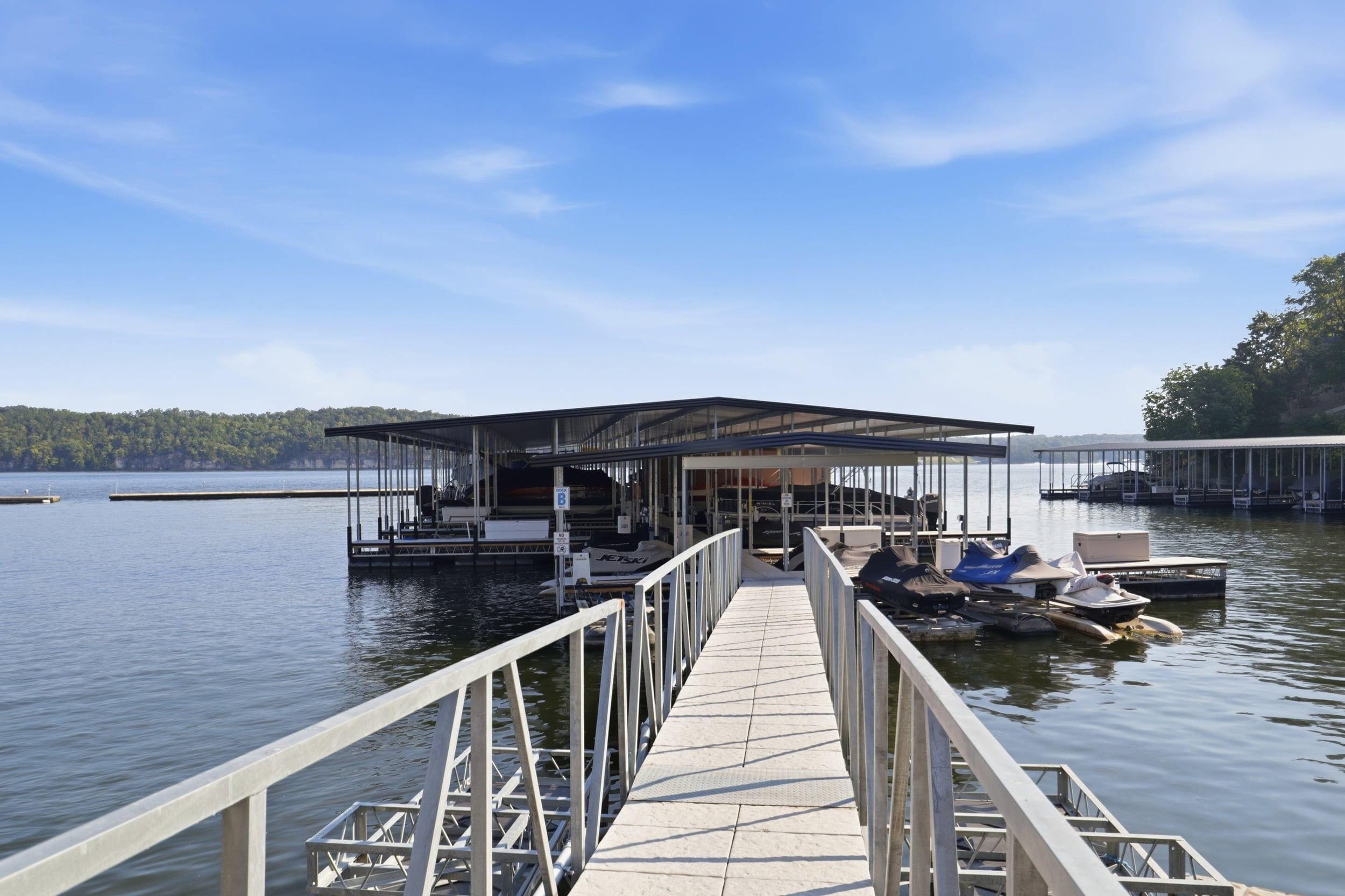 Um cais leva a um barco coberto, com vista para o lago e colinas arborizadas ao fundo.