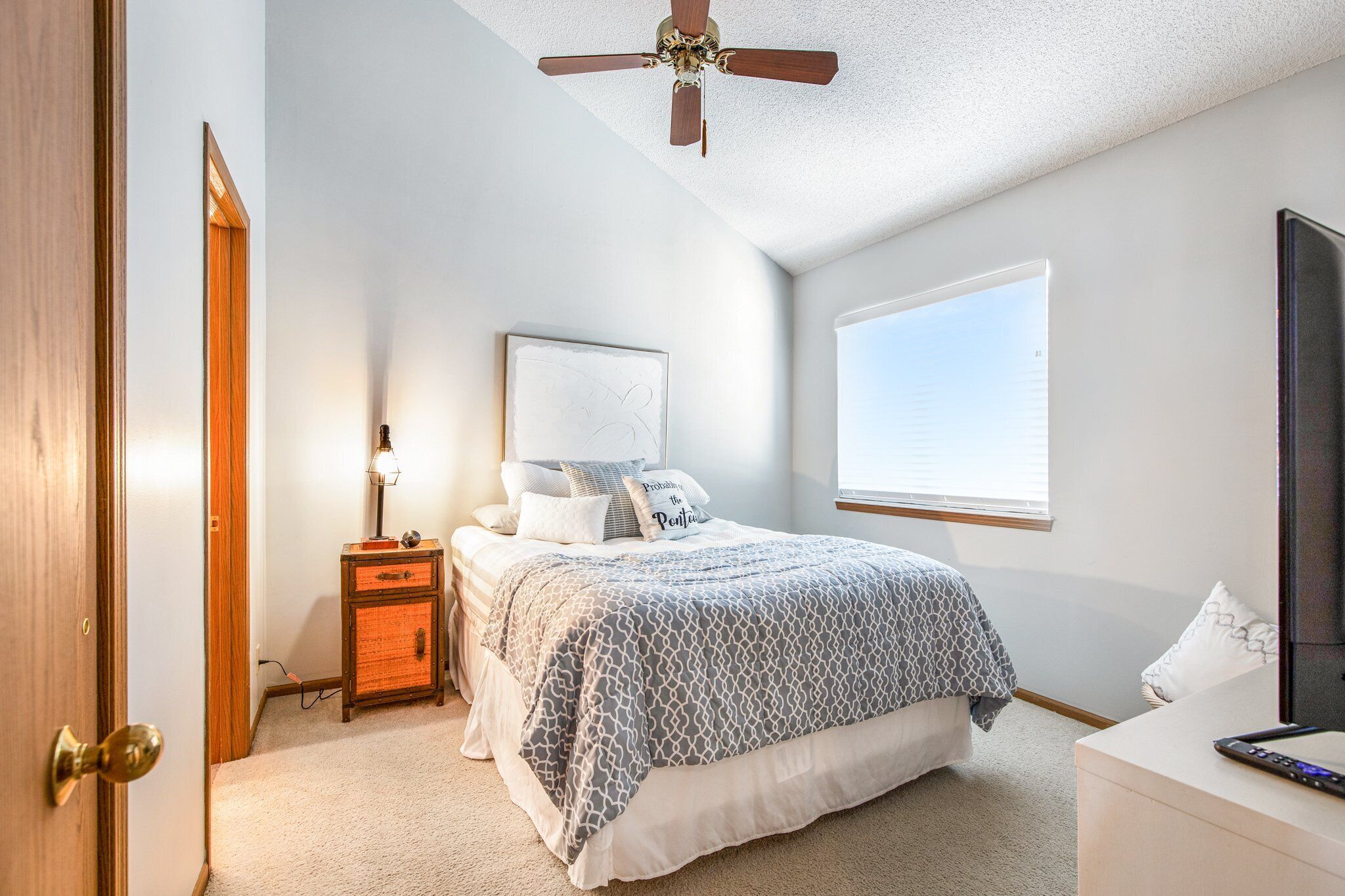 A bedroom with a bed, bedside table, lamp, and a ceiling fan.