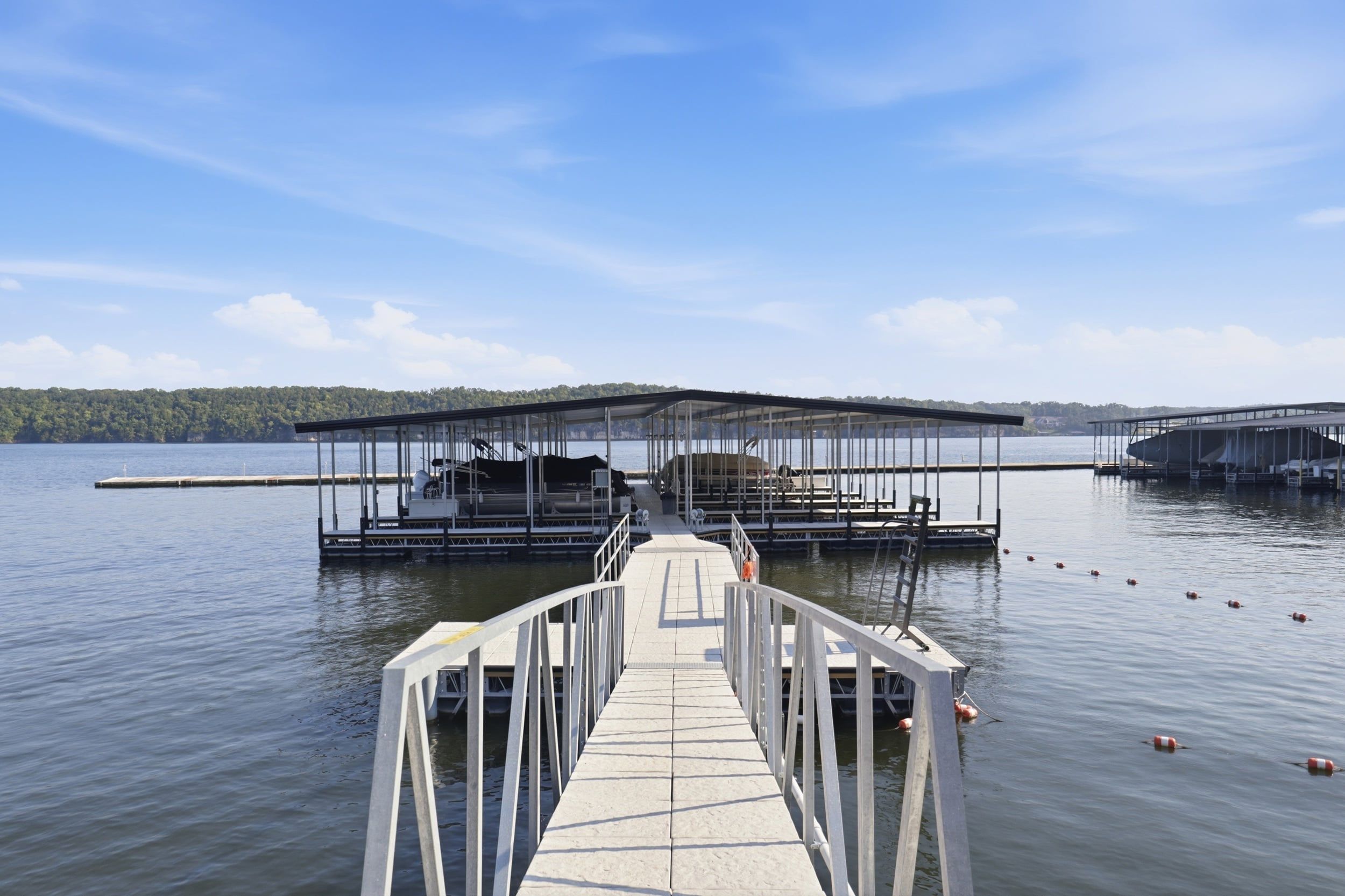A pier leading to a dock with a covered boat area and a view of a lake and forested land.
