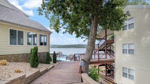 A wooden pathway leading to a dock with a sign, a pool, and a lake view. - Poolside Condo With Amazing Lake Views & Design (Osage Beach)