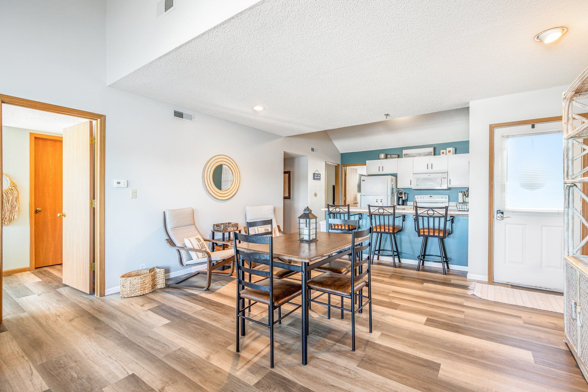 A spacious dining area with a wooden table and chairs, a kitchen in the background, and a view of the outdoors.