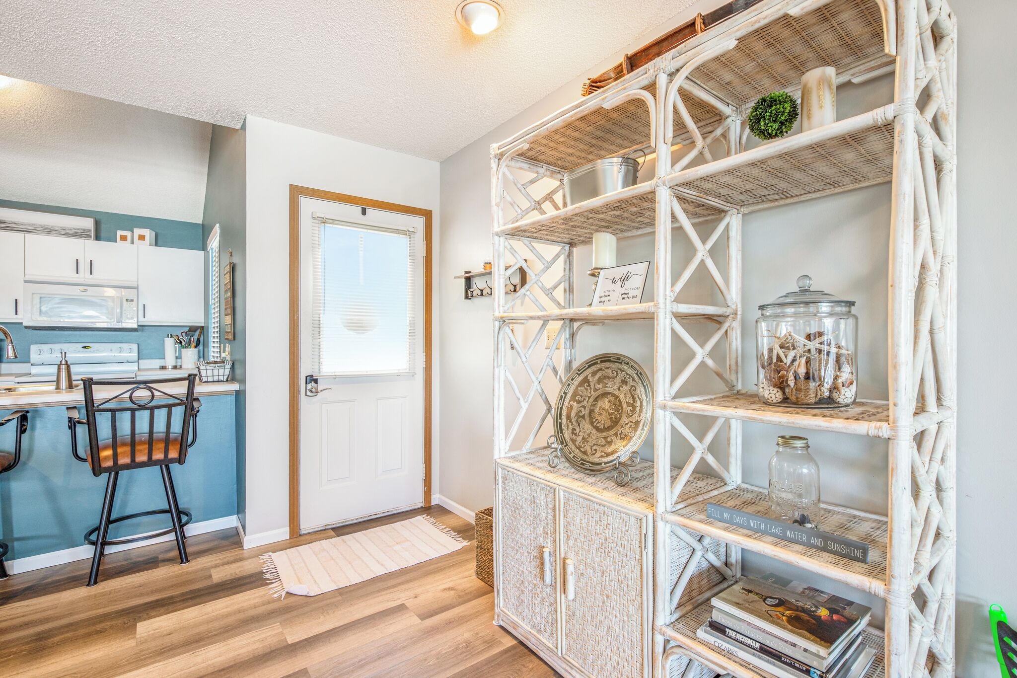 A kitchen with white cabinets, a microwave, and a wicker shelf unit with decorative items.