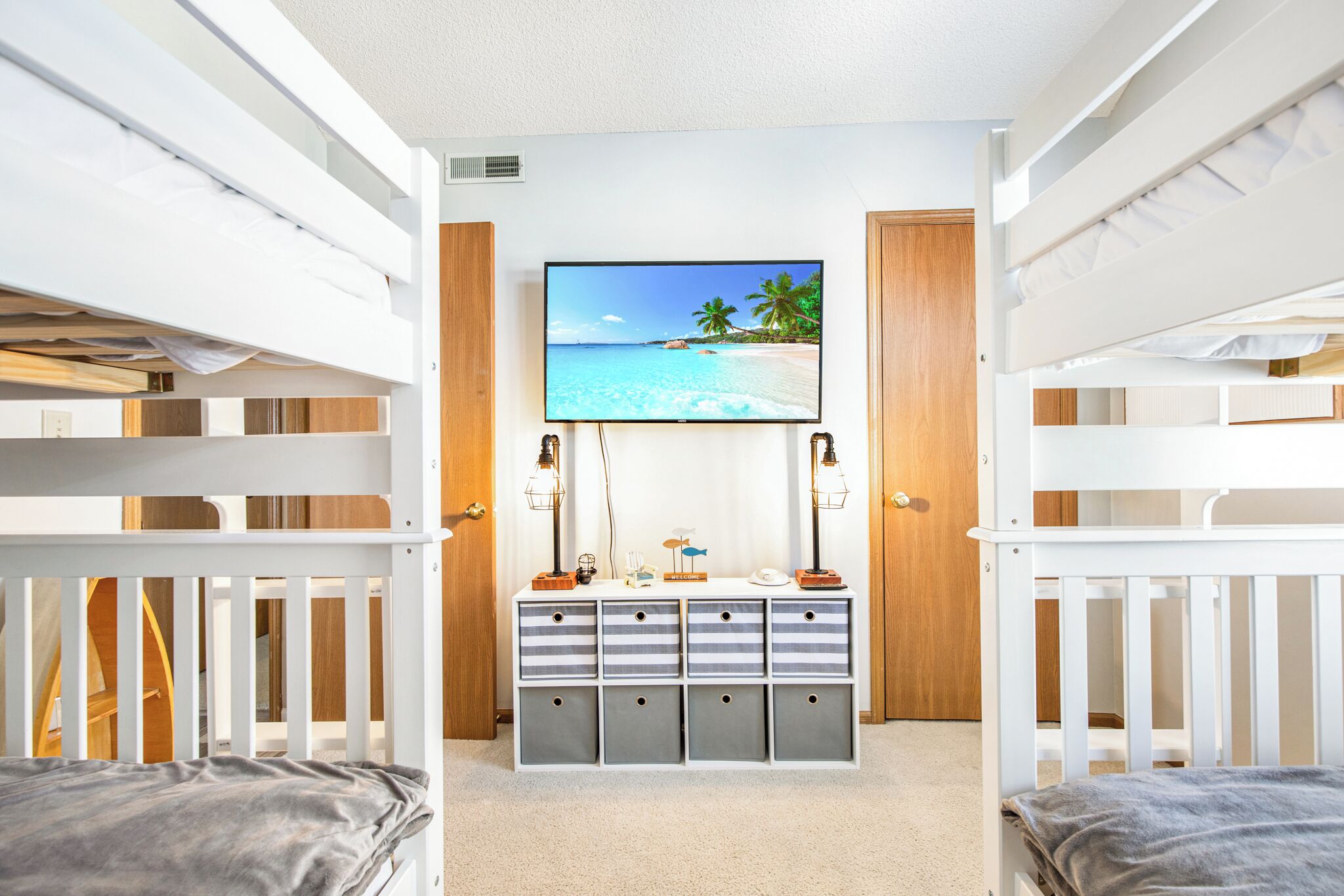 Quarto com beliches, televis ão presa na parede e um móvel com gavetas.