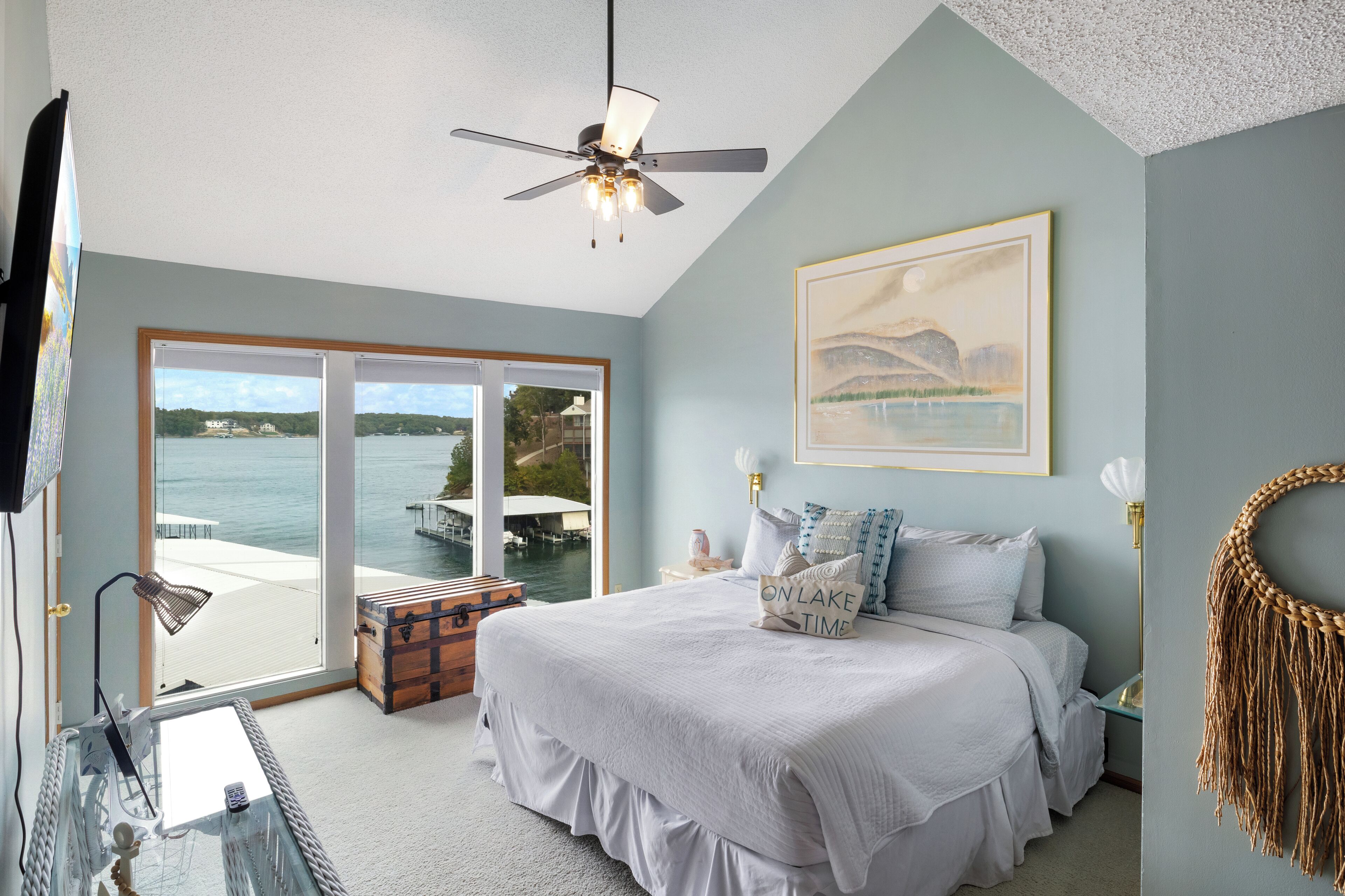 Ein Schlafzimmer mit einem großen Bett, einem Deckenventilator, Blick auf das Wasser und einer hölzernen Truhe.