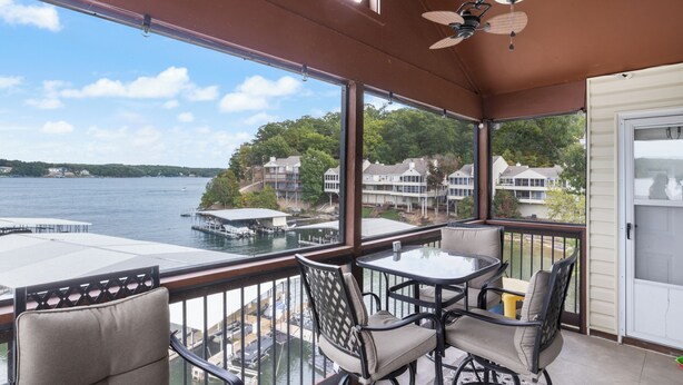 A balcony with a table and chairs, overlooking a body of water and houses. - Poolside Condo With Amazing Lake Views & Design (Osage Beach)