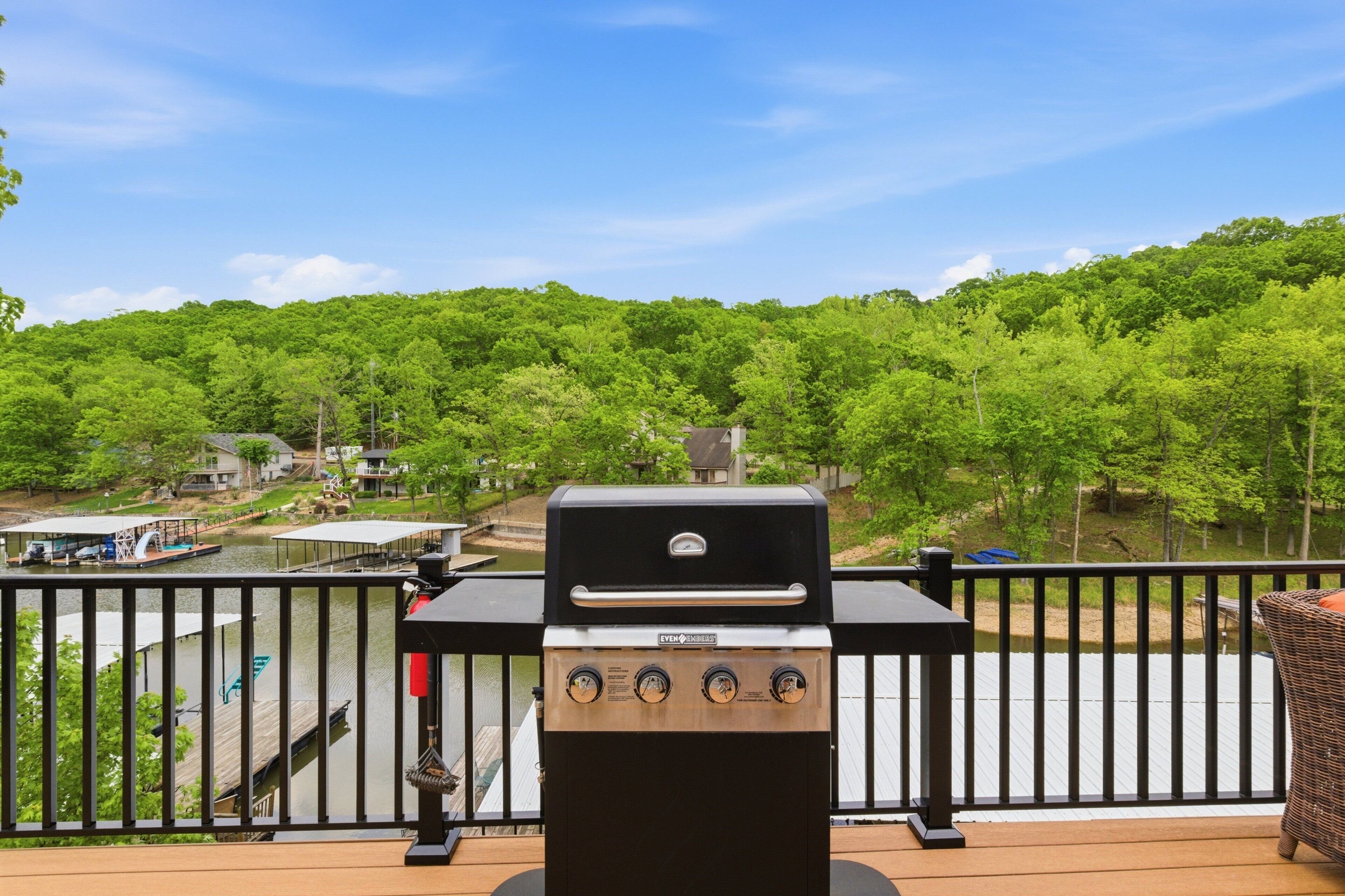 A grill on a deck with a view of a lake and forest.