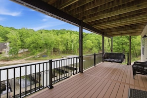 A covered deck with a railing, a bench, and a view of a river and forest.