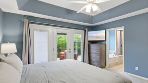 Ein Schlafzimmer mit Bett, Kommode, Fernseher und Blick ins Freie.