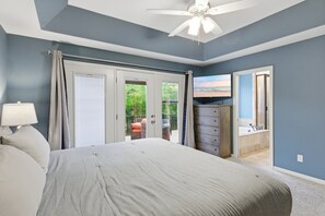 A bedroom with a bed, a dresser, a television, and a view of the outdoors.