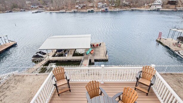 A deck with wooden chairs and a table overlooking a calm lake with docks and boats. - Lake Life: Amazing Weekday Specials! Dock, Swim Mat, Cove Water (Eldon)