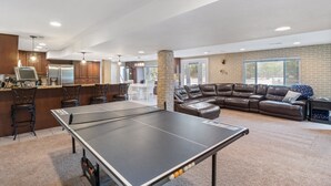A spacious living area with a ping pong table, a brown leather couch, and a kitchen in the background. - Lake Life: Amazing Weekday Specials! Dock, Swim Mat, Cove Water (Eldon)