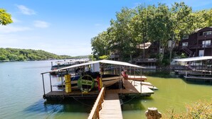 A dock with a boat, a lifebuoy, and a wooden walkway leading to a building with balconies.