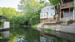 A house with a dock extending into a calm lake, surrounded by lush greenery.