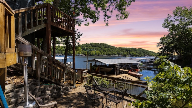 A wooden deck with outdoor seating, a metal grill, and a view of a lake and dock area.