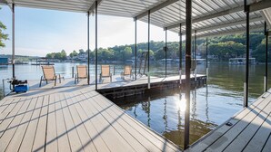 Eine überdachte Terrasse mit Stühlen und ein Steg, der in einen ruhigen See führt, umgeben von Bäumen und Gebäuden.
