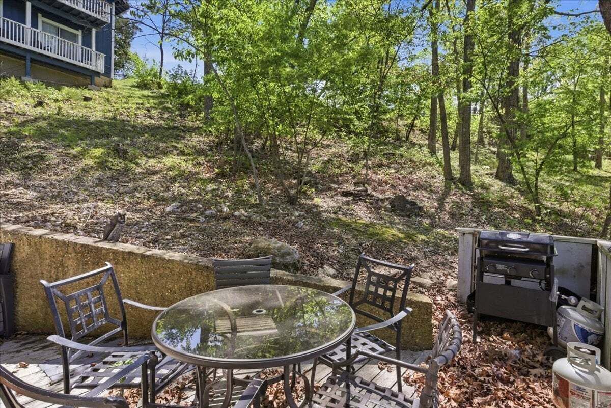 A patio with a glass table and chairs, a barbecue grill, and a stone wall.