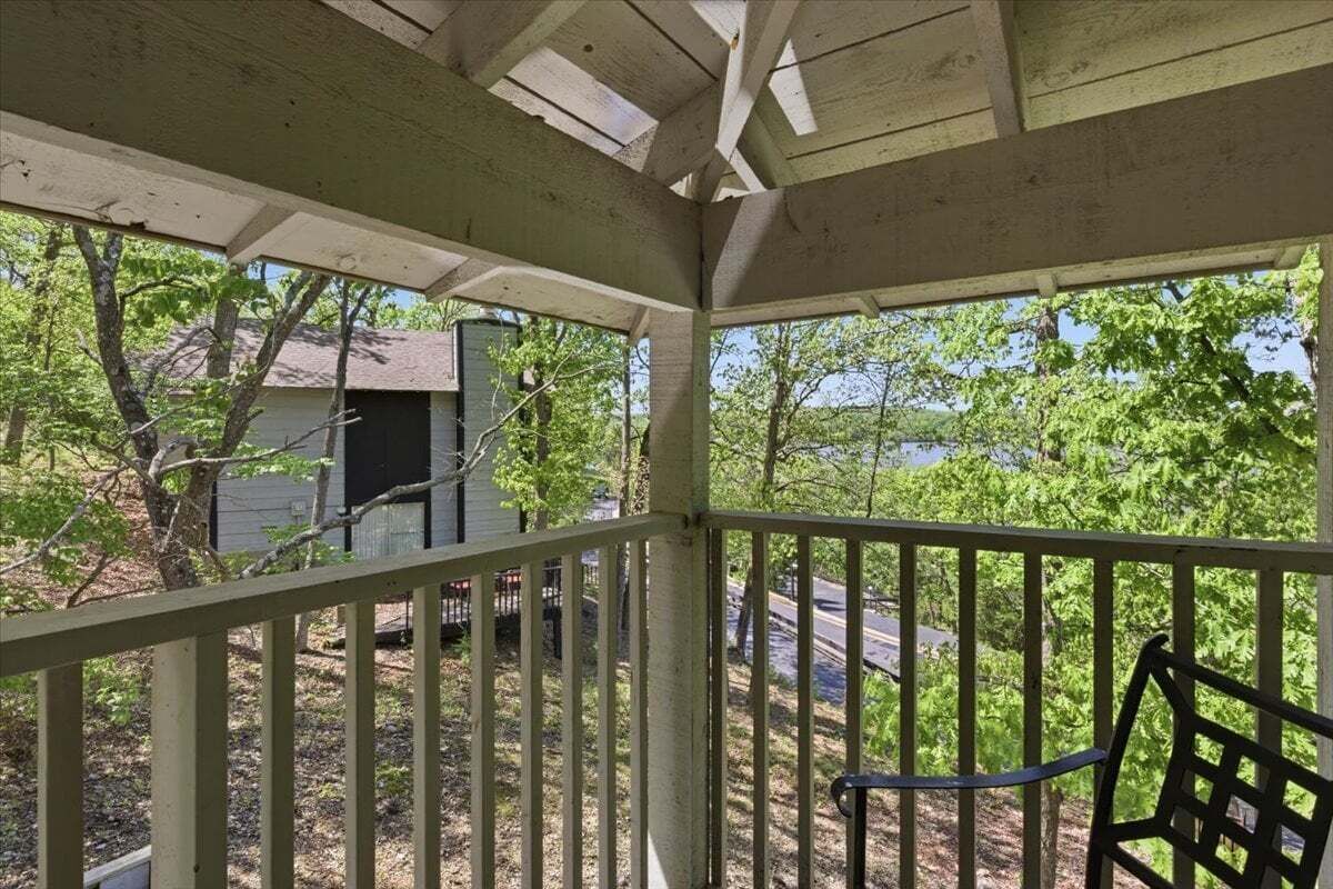 Eine überdachte Veranda mit Geländer, eine kleine Gartenhütte im Hintergrund und Bäume ringsum.