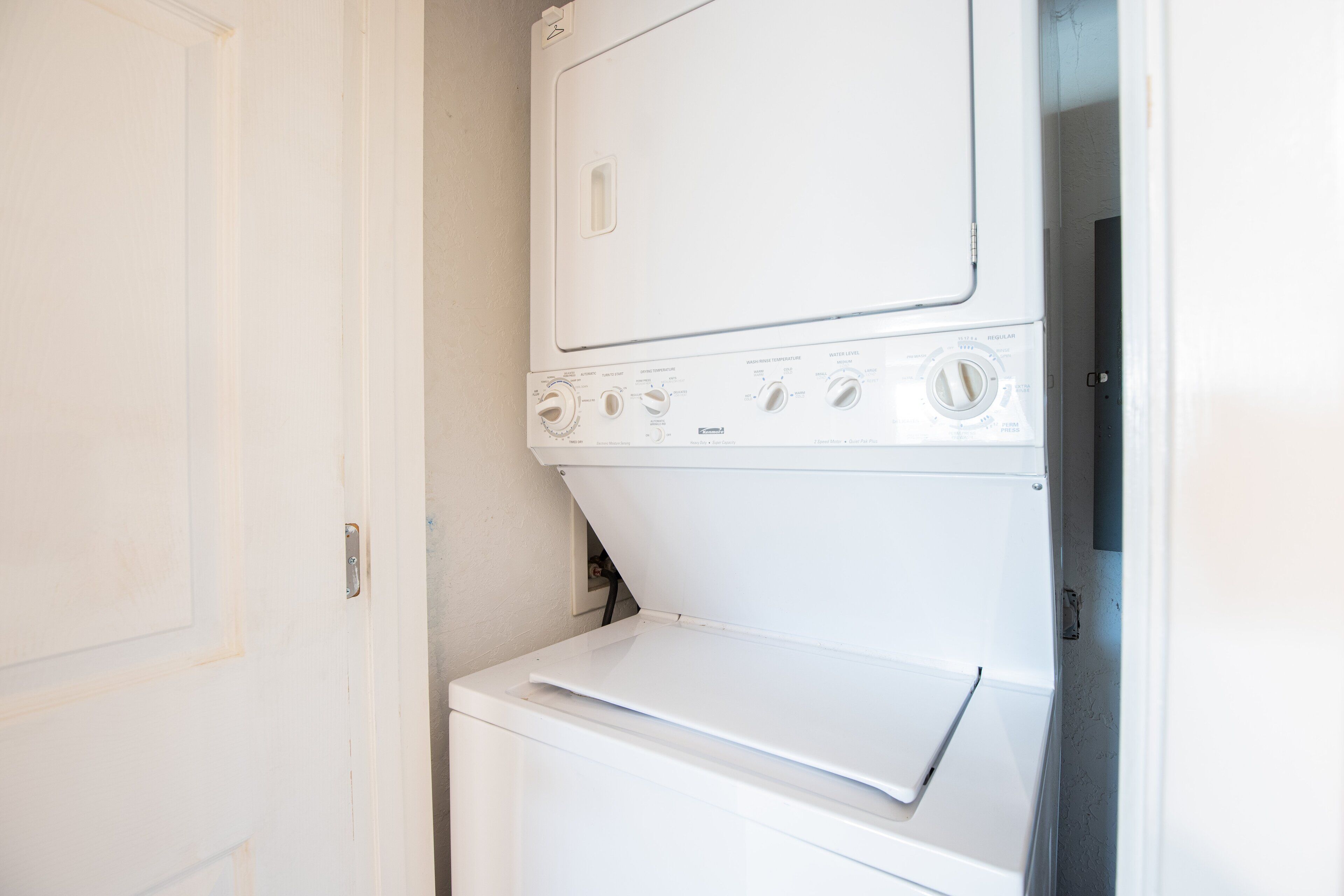 A compact, white, wall-mounted washer and dryer unit with multiple control knobs and settings.