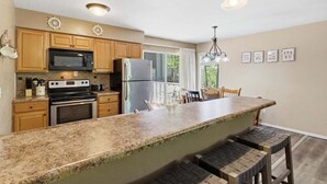 A kitchen with wooden cabinets, a granite countertop, a stainless steel refrigerator, and a large island with bar stools. - Great Location, Margaritaville Amenities & Hot Tub (Osage Beach)