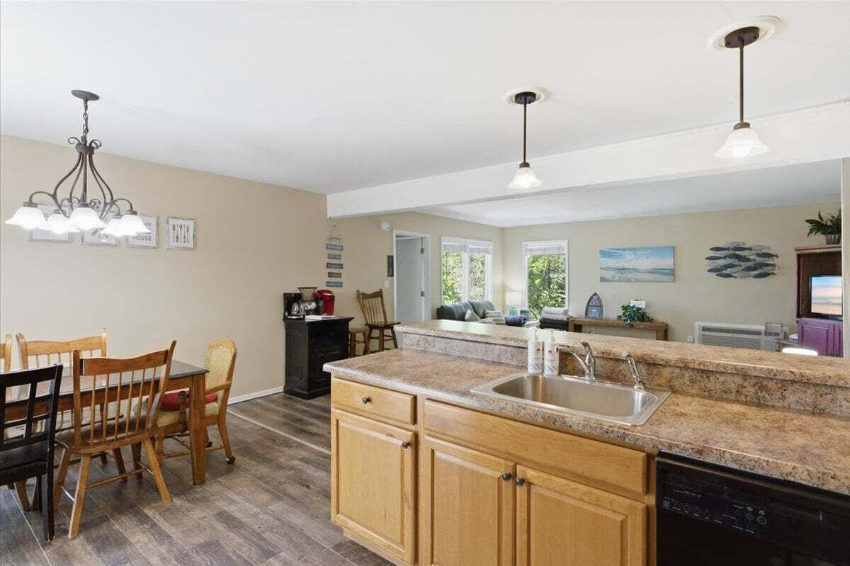 A kitchen with granite countertops, wooden cabinets, a dishwasher, a dining area with a table and chairs, and pendant lighting.