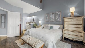 Une chambre à coucher avec un grand lit, une commode, une coiffeuse avec un miroir et des œuvres d’art décoratives au mur.