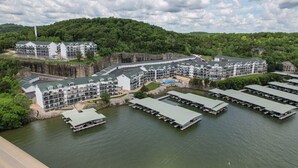 Un hôtel situé au bord de l’eau, composé de plusieurs bâtiments, avec des bateaux amarrés et une colline boisée en arrière-plan.